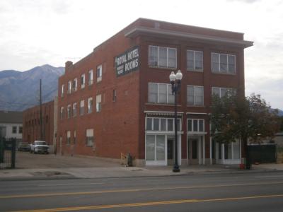 A multi-story red brick building with a painted "Royal Hotel" sign on its side, situated on a street corner with a mountain range visible in the background.