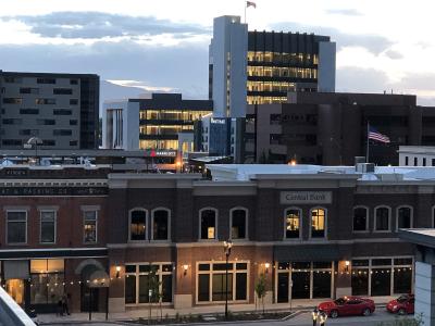 A view of a downtown streetscape at dusk, featuring a brick building with a "Central Bank" sign, a Marriott hotel, and a tall white office building, with the Wasatch Mountains visible in the background.