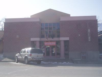 The image shows the exterior facade of a single-story building with a beige stucco upper section and a reddish-brown brick lower section, featuring a central entrance with glass doors, a large window, and the text "DAN O'L AURIE MUSEUM" mounted above
