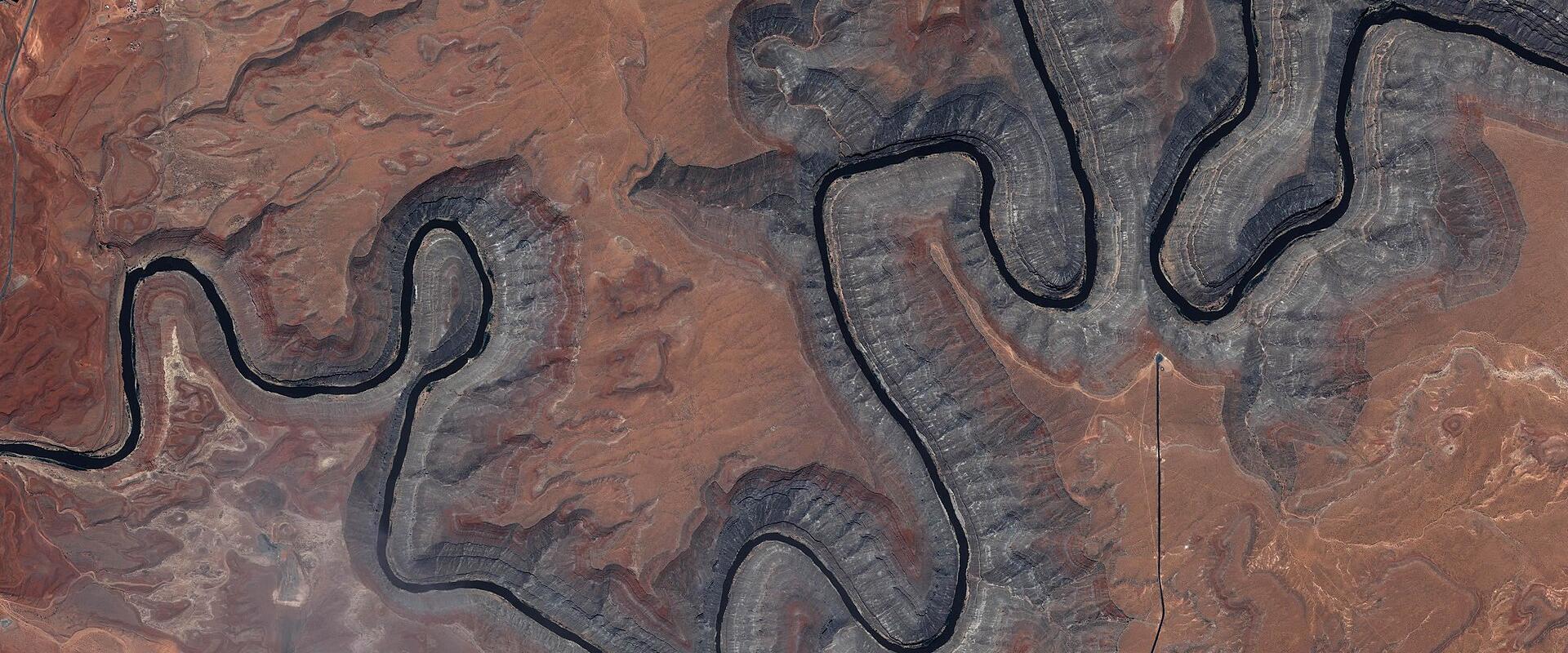 An aerial satellite view of a river forming deep, tight meanders through reddish-brown desert terrain, identified by the filename as Goosenecks State Park.
