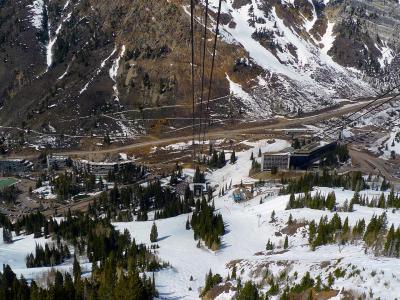 A high-angle view looking down from a ski lift onto a large, multi-story hotel complex (the Jughandle) and surrounding lodge buildings, with steep, snow-dusted mountain slopes in the background.