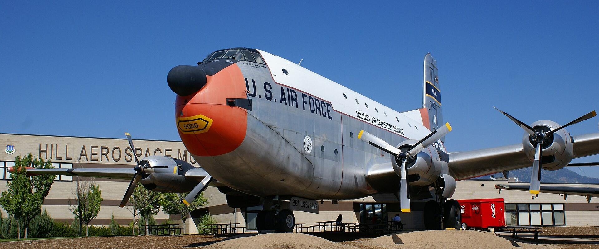 A Douglas C-124 Globemaster II aircraft displayed outdoors on a gravel pad with a building in the background.