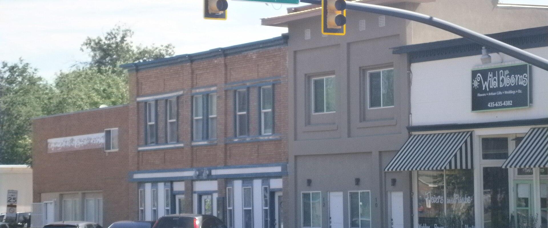 A street-level view of a row of commercial buildings at an intersection marked by a green street sign reading "STATE STREET" and traffic lights.