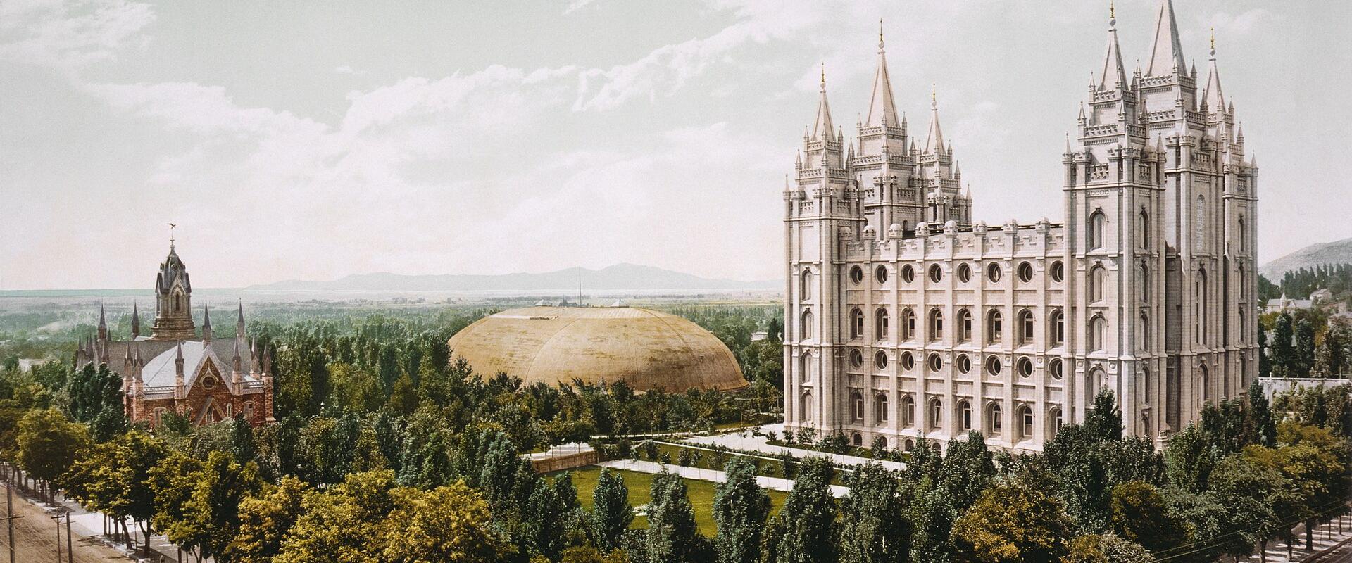 The image shows a high-angle, colorized view of a large, ornate white building with multiple spires (the Salt Lake Temple) and a separate, smaller brick structure with a steeple (the Assembly Hall) to the left, set within a landscaped park with a lar