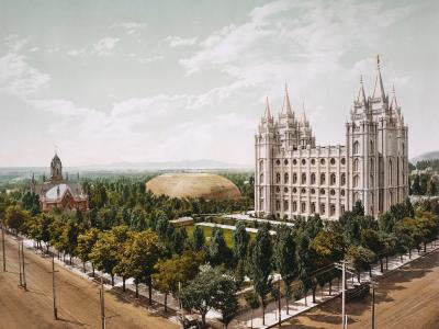 The image shows a high-angle, colorized view of a large, ornate white building with multiple spires (the Salt Lake Temple) and a separate, smaller brick structure with a steeple (the Assembly Hall) to the left, set within a landscaped park with a lar