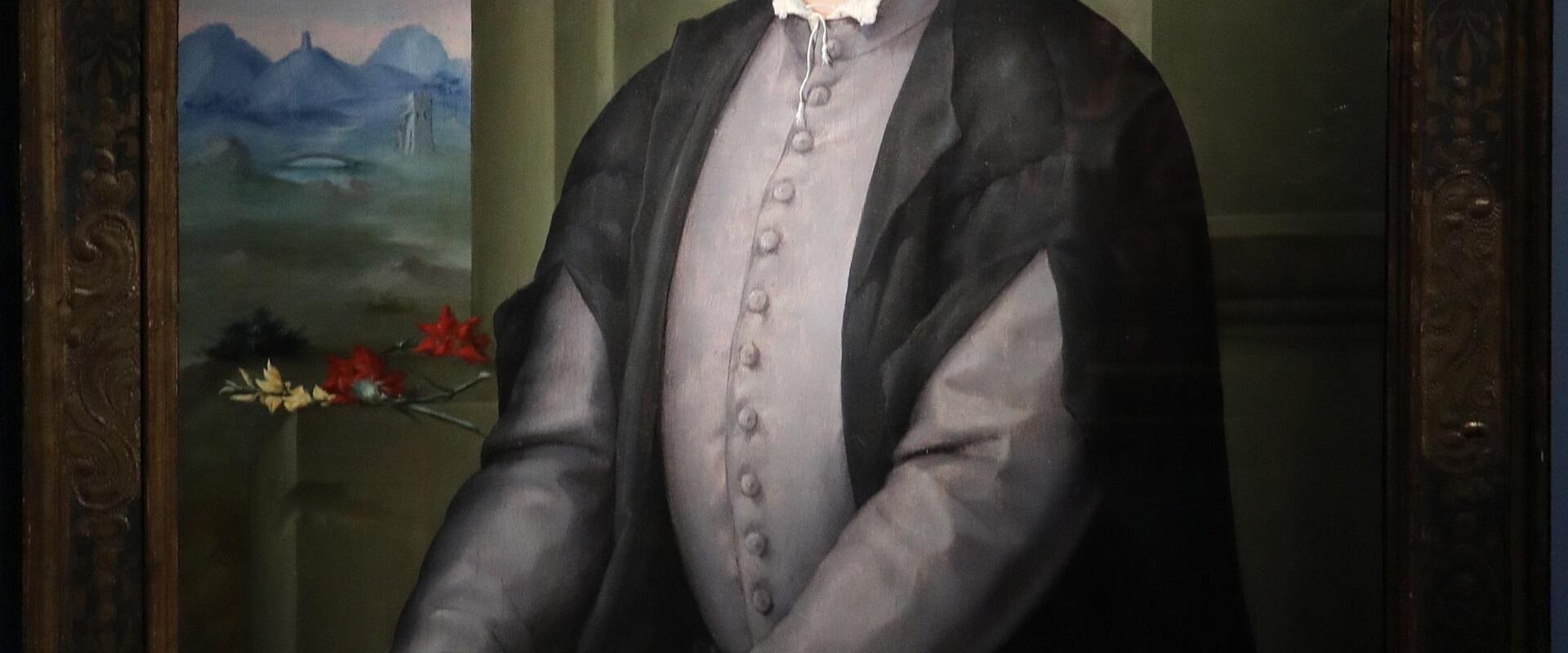 A framed Renaissance-style portrait painting of a young man in a black cap and grey doublet, holding a floral wreath, set against a landscape background.