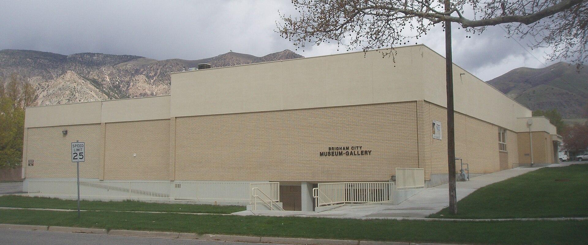 The image shows a single-story, beige brick building with a flat roof, situated next to a street.
