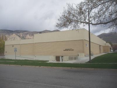 The image shows a single-story, beige brick building with a flat roof, situated next to a street.