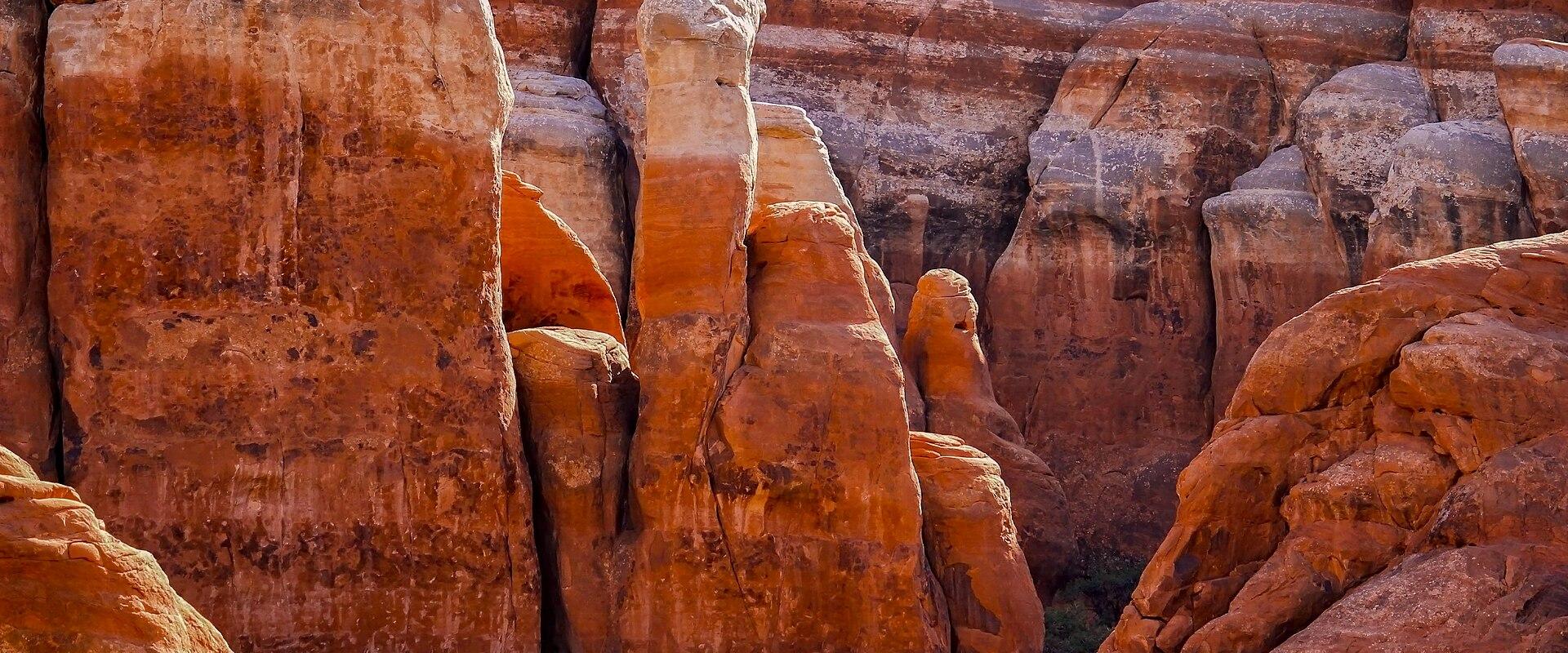 Close-up view of red sandstone rock formations, specifically a tall, thin fin or spire, with other layered rock formations in the background.
