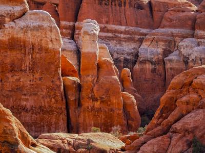Close-up view of red sandstone rock formations, specifically a tall, thin fin or spire, with other layered rock formations in the background.