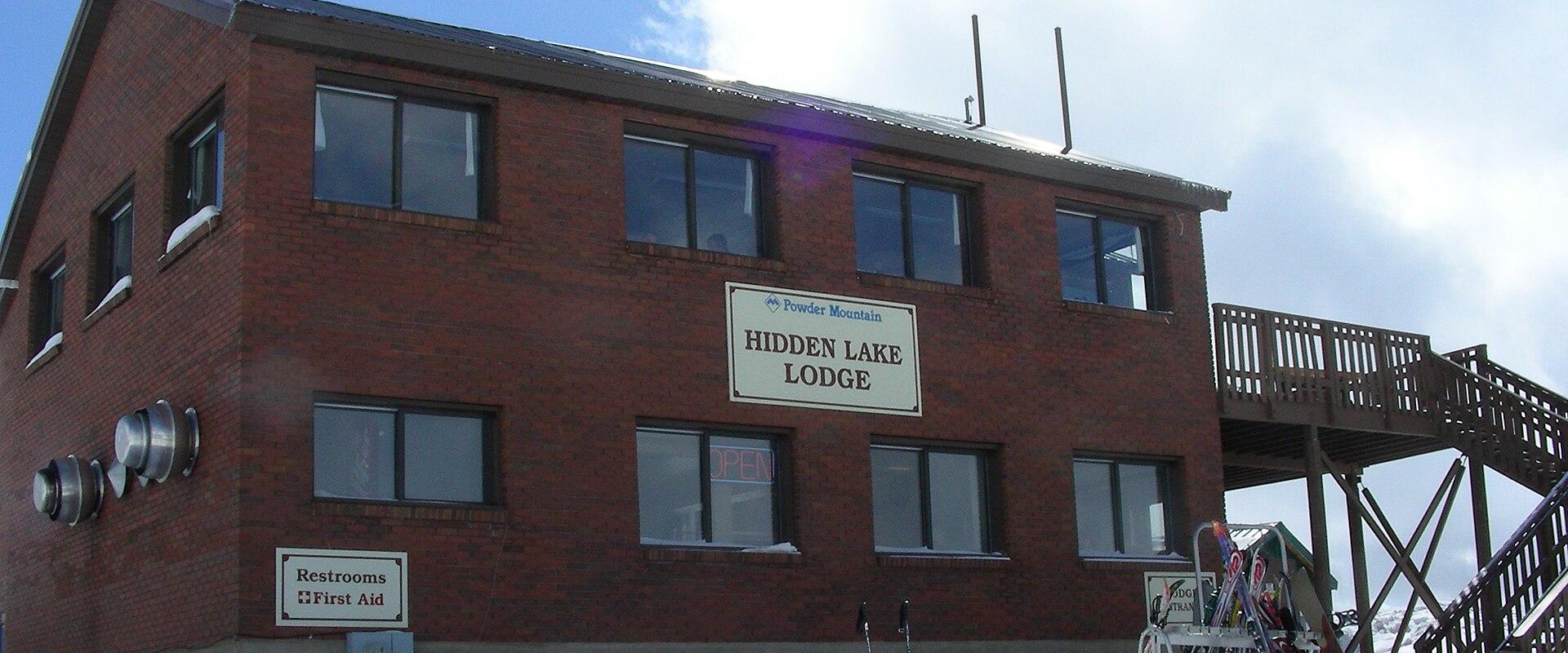 A two-story brick building with a sign reading "Powder Mountain Hidden Lake Lodge" and a smaller sign for "Restrooms / First Aid"