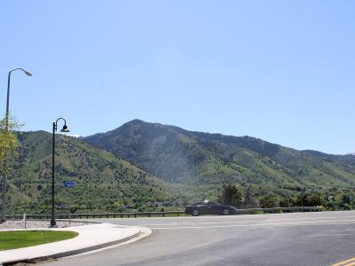 A view of a green, rolling mountain range with a paved road in the foreground, a black car, and a street lamp on the left.