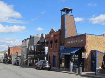 A street-level view of a brick building with a blue awning, identified by large lettering on the facade as the "Park City Museum," situated on a street with other buildings and a parked car.