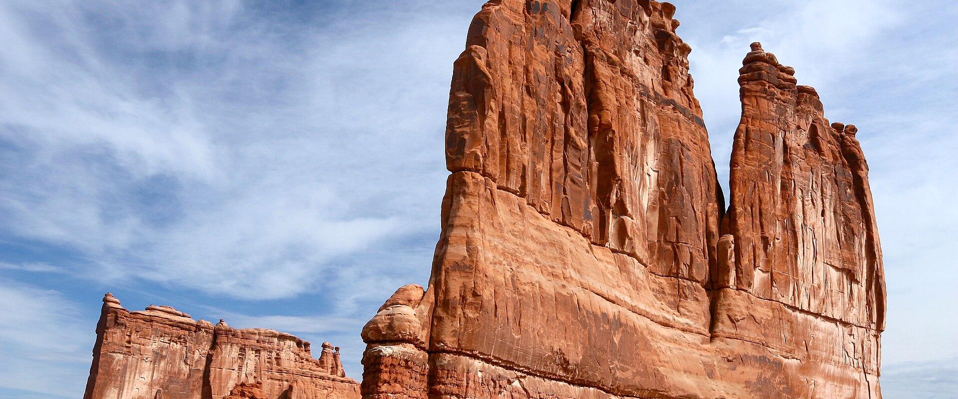 The image shows a large, distinctive red sandstone rock formation known as "The Organ," located alongside a paved road with a white vehicle visible in the lower left corner.